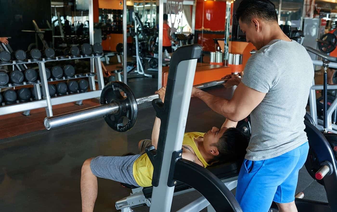 Fitness Trainer helps guy heavy lifting